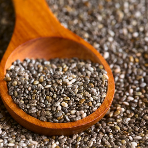 Chia seeds in a wooden spoon, surrounded by scattered chia seeds where we make oil off.